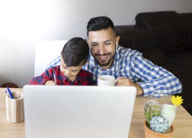 Baba oğluyla evde video konferansına ev ödevi yapıyor.