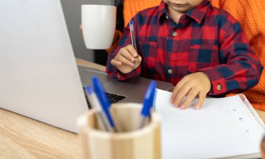 Çocuk annesiyle birlikte evde dizüstü bilgisayarla ödev yapıyor.