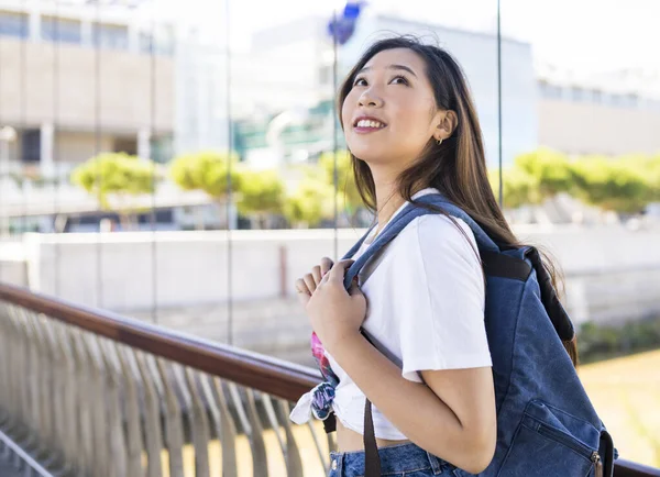 Japanese woman with a backpack outdoors, looking up