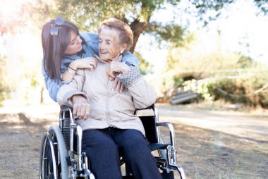 Tekerlekli sandalyede yaşlı bir kadınla genç bir kız, mutlu bir gülüş.