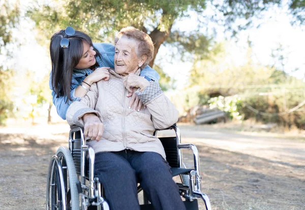 Tekerlekli sandalyede yaşlı bir kadınla genç bir kız, mutlu bir gülüş.