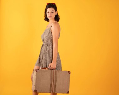 Bavullu kadın sarı arka planda seyahat etmeye hazır.