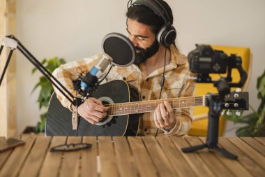 Evde mikrofon ve kulaklıkla gitar çalan bir adam nüfuzlu kayıt, podcast blogcusu