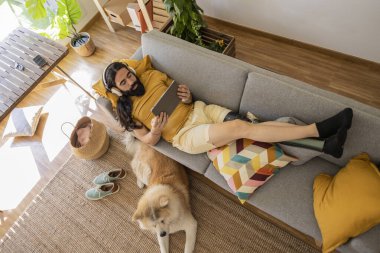 Dijital tablete bakarken kanepede köpeğinin yanında uzanan adamın biyonik bir bacağı var.