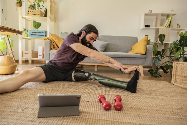 man amputated leg prosthesis, sport at home online class doing stretching and weight training