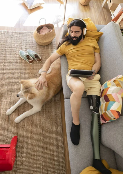 bionic leg man lying on sofa with his dog watching movie on digital tablet