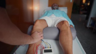 Experienced physical therapist placing needles on a patient's leg and connecting electrodes for an electroacupuncture session, a modern approach to traditional chinese medicine for pain relief