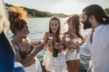 Eğlence teknesinde kutlama yapan, gün batımında şampanyayla kadeh kaldıran, yaz tatili boyunca kahkaha atan ve mutlu anlarını paylaşan bir grup arkadaş.