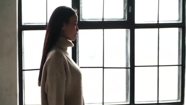 Steadicam shot of a young beautiful Asian girl in a great mood on the way to work. Model of Asian appearance, in a long sweater walks in front of the window of a beautiful loft. Slow motion. Average — Stock Video