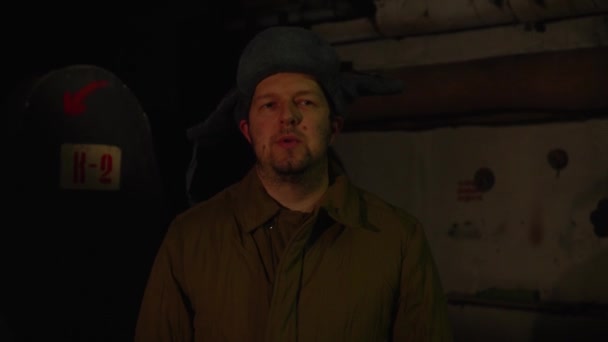 Hombre ruso en un sombrero con orejeras, hablando por teléfono en un sótano oscuro y decide asuntos de importancia nacional . — Vídeo de stock