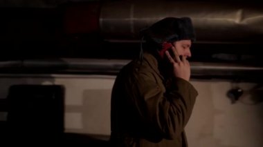 Kulak lık şapkalı Rus adam, karanlık bir bodrumda telefonda konuşuyor ve ulusal öneme sahip konulara karar veriyor..
