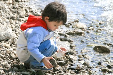 Çakıl taşları ile kumsalda oynarken küçük çocuk.