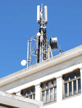 Cell phone telecommunications antennas and repeaters on building against clear blue sky clipart