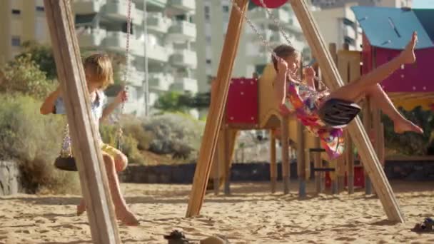 Happy children swinging outdoors. Boy and girl have fun on playground. — Stock Video