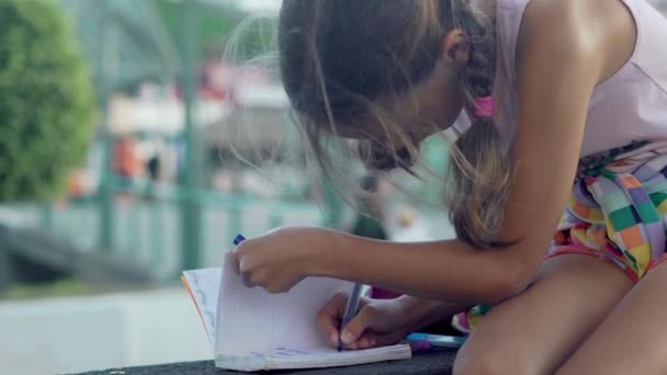 Menina escreve em um caderno e estudar outdors . — Vídeo de Stock