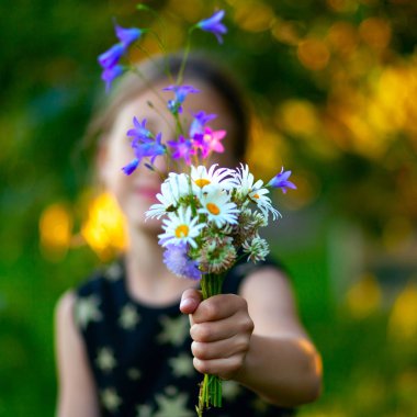 Kır çiçekleri buketi ile küçük sevimli kız. Çocuk anneme çiçek verir. Mevcut elin yukarı görünümünü kapat.