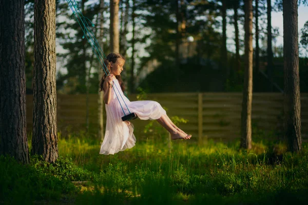 Happy child girl on swing in pink dress in the forest. Summertime. — Stock Photo, Image