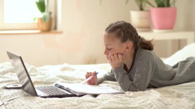 Tatlı çocuk eğitim için dizüstü bilgisayar kullanıyor, online öğrenim görüyor, evde eğitim görüyor. Kızın evde ödevi var..