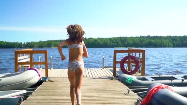 Flicka i våtdräkt hoppar ner i sjön från träpiren. Ha kul på sommardagen. — Stockvideo