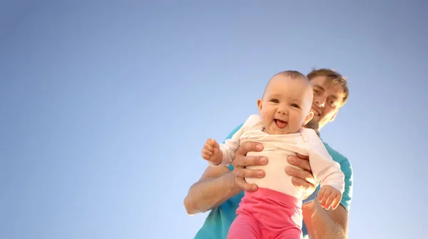 Ojciec trzyma małe dziecko w ramionach na tle letniego błękitnego nieba. Słodkie dziecko się uśmiecha. Szczęśliwa rodzina na świeżym powietrzu. — Zdjęcie stockowe