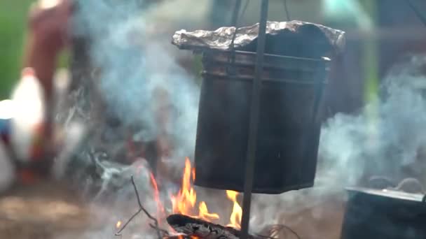 Förbereder mat på lägereld. Vattenkokare med läcker färsk soppa brinner i rök — Stockvideo