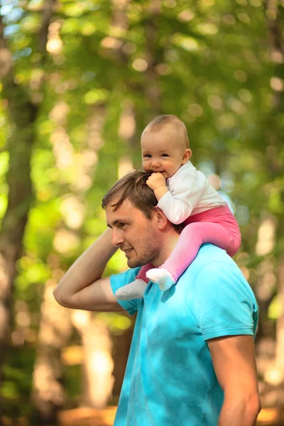 Dziecko siedzi na ramionach swoich ojców. Ojciec i dziecko spacerujący po parku. Czas letni. Szczęśliwa rodzina. — Zdjęcie stockowe