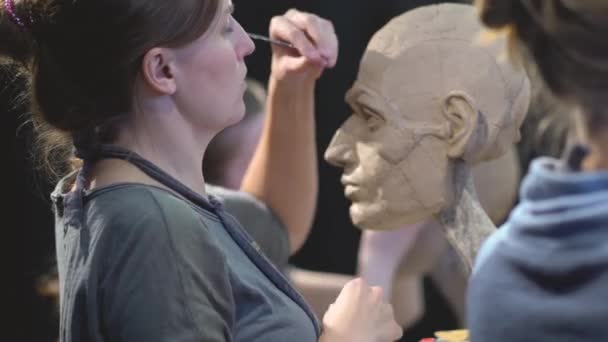 Vrouw beeldhouwer aan het werk op een sculptuur van een menselijk hoofd. — Stockvideo