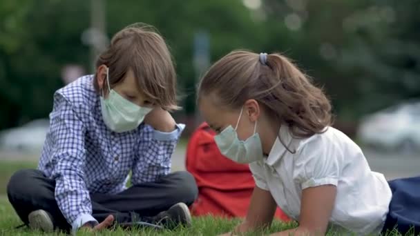 초등 학교에서 스마트폰을 사용하는 귀여운 학생들. 안전 마스크를 쓴 소년 소녀와 소녀의 손에 기구를 들고 있는 모습. — 비디오