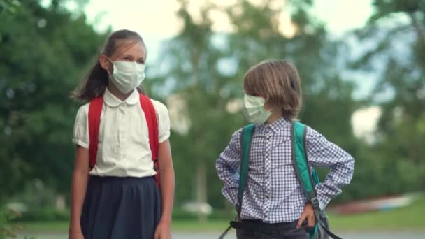 A gyerekek visszamennek az iskolába. Aranyos tanulók hátizsákkal. Fiú és lány biztonsági maszkban. — Stock videók