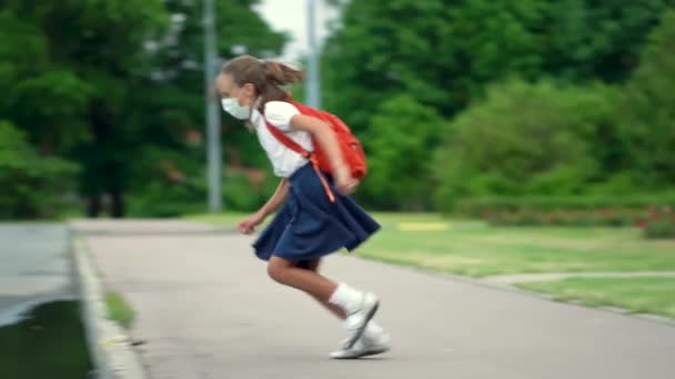 A criança volta para a escola. Aluno bonito com mochila. Menina em máscaras de segurança pulando sobre uma poça — Vídeo de Stock