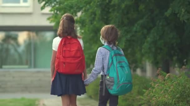 As crianças voltam para a escola. Pupilas giras com mochilas. Menino e menina em máscaras de segurança — Vídeo de Stock