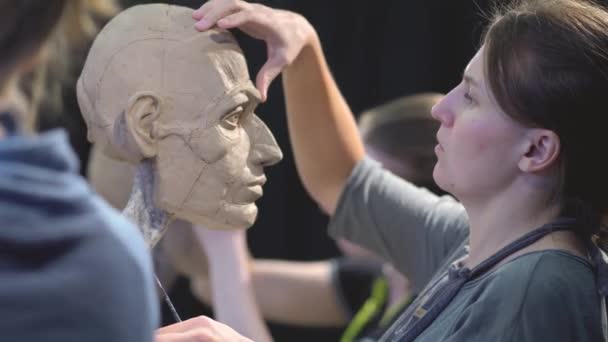 Vrouw beeldhouwer aan het werk op een sculptuur van een menselijk hoofd. — Stockvideo