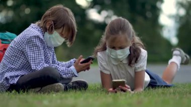 İlkokulda akıllı telefon kullanan sevimli öğrenciler. Güvenlik maskeli bir çocuk ve kız ellerinde aletlerle..