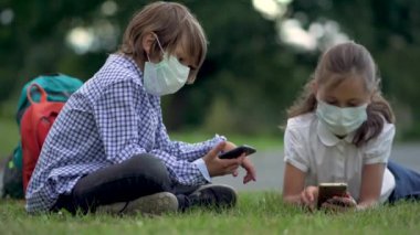 İlkokulda akıllı telefon kullanan sevimli öğrenciler. Güvenlik maskeli bir çocuk ve kız ellerinde aletlerle..
