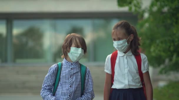 Los niños vuelven a la escuela. Lindos alumnos con mochilas. Niño y niña con máscaras de seguridad — Vídeo de stock