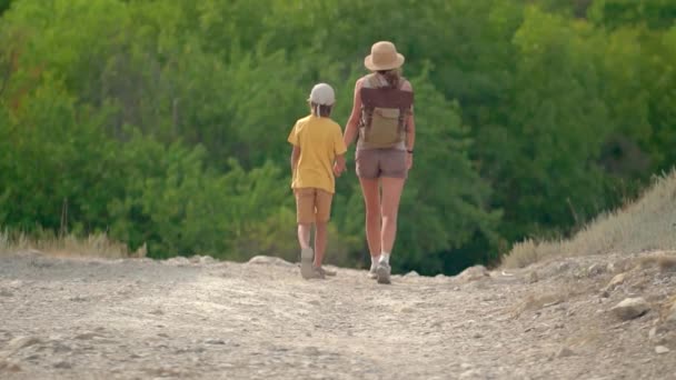 Femme avec sac à dos marchant avec son fils sur la route dans les montagnes. Voyage style de vie concept aventure vacances d'été en plein air. — Video