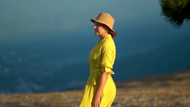 Vacker ung kvinna i gul klänning står på en klippa av ett berg. Klänningen och håret fladdrar i vinden. — Stockvideo