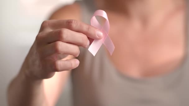 Una donna tiene il nastro rosa. Vista ravvicinata della mano con simbolo del mese nazionale di sensibilizzazione al cancro al seno in ottobre — Video Stock