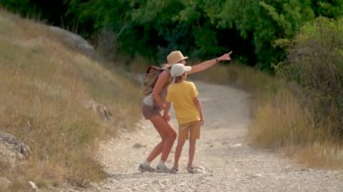 Sırt çantalı bir kadın oğluyla dağlarda yolda yürüyor. Seyahat yaşam tarzı konsept macera açık hava yaz tatilleri.
