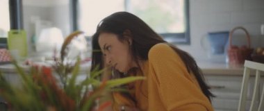 Evdeki mutfak masasında otururken üzgün, üzgün ve incinmiş hisseden genç bir kadın. Ayrılmak, aşk, nefret, boşanma kavramı. Sığ DOF, Yavaş çekim, BMPCC 4K