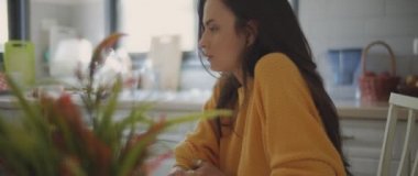 Evdeki mutfak masasında otururken üzgün, üzgün ve incinmiş hisseden genç bir kadın. Ayrılmak, aşk, nefret, boşanma kavramı. Sığ DOF, Yavaş çekim, BMPCC 4K