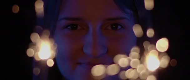 一个女人在镜头前微笑 面前闪烁着两个火花 蓝色工作室照明 庆祝概念 慢动作 浅层Dof Bmpcc — 图库视频影像