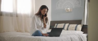 Evden bir dizüstü bilgisayarla çalışırken telefonda biriyle konuşan bir kadın. Ağır çekim, BMPCC 4K