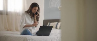 Evden bir dizüstü bilgisayarla çalışırken telefonda biriyle konuşan bir kadın. Ağır çekim, BMPCC 4K