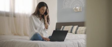 Evden bir dizüstü bilgisayarla çalışırken telefonda biriyle konuşan bir kadın. Ağır çekim, BMPCC 4K