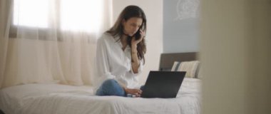 Evden bir dizüstü bilgisayarla çalışırken telefonda biriyle konuşan bir kadın. Ağır çekim, BMPCC 4K