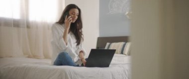 Evden bir dizüstü bilgisayarla çalışırken telefonda biriyle konuşan bir kadın. Ağır çekim, BMPCC 4K