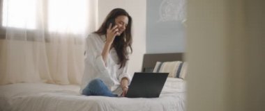 Evden bir dizüstü bilgisayarla çalışırken telefonda biriyle konuşan bir kadın. Ağır çekim, BMPCC 4K