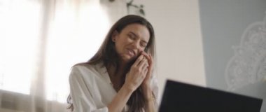 Beyaz tişörtlü bir kadının evden bilgisayarla uğraşırken telefonla konuştuğu bir fotoğraf. Ağır çekim, BMPCC 4K