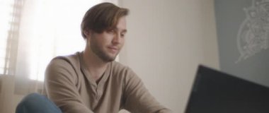 Yatakta oturup bilgisayarla çalışan genç bir adamın yakın çekimi. Ağır çekim, BMPCC 4K